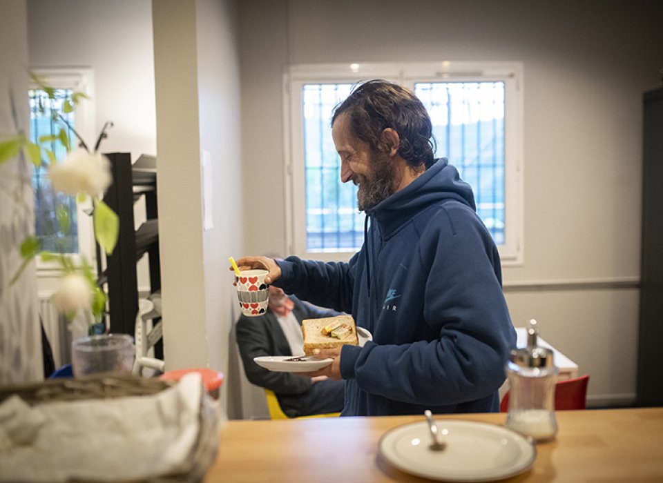 Un homme sourit, un café à la main, à l'accueil de jour de la Voûte.