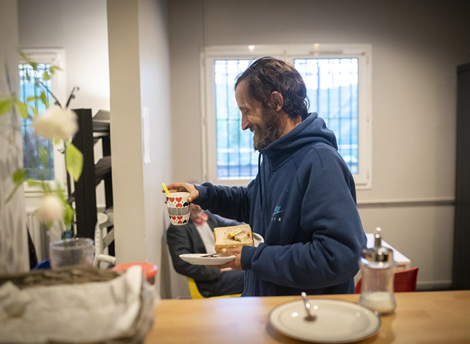 Un homme sourit, un café à la main, à l'accueil de jour de la Voûte.
